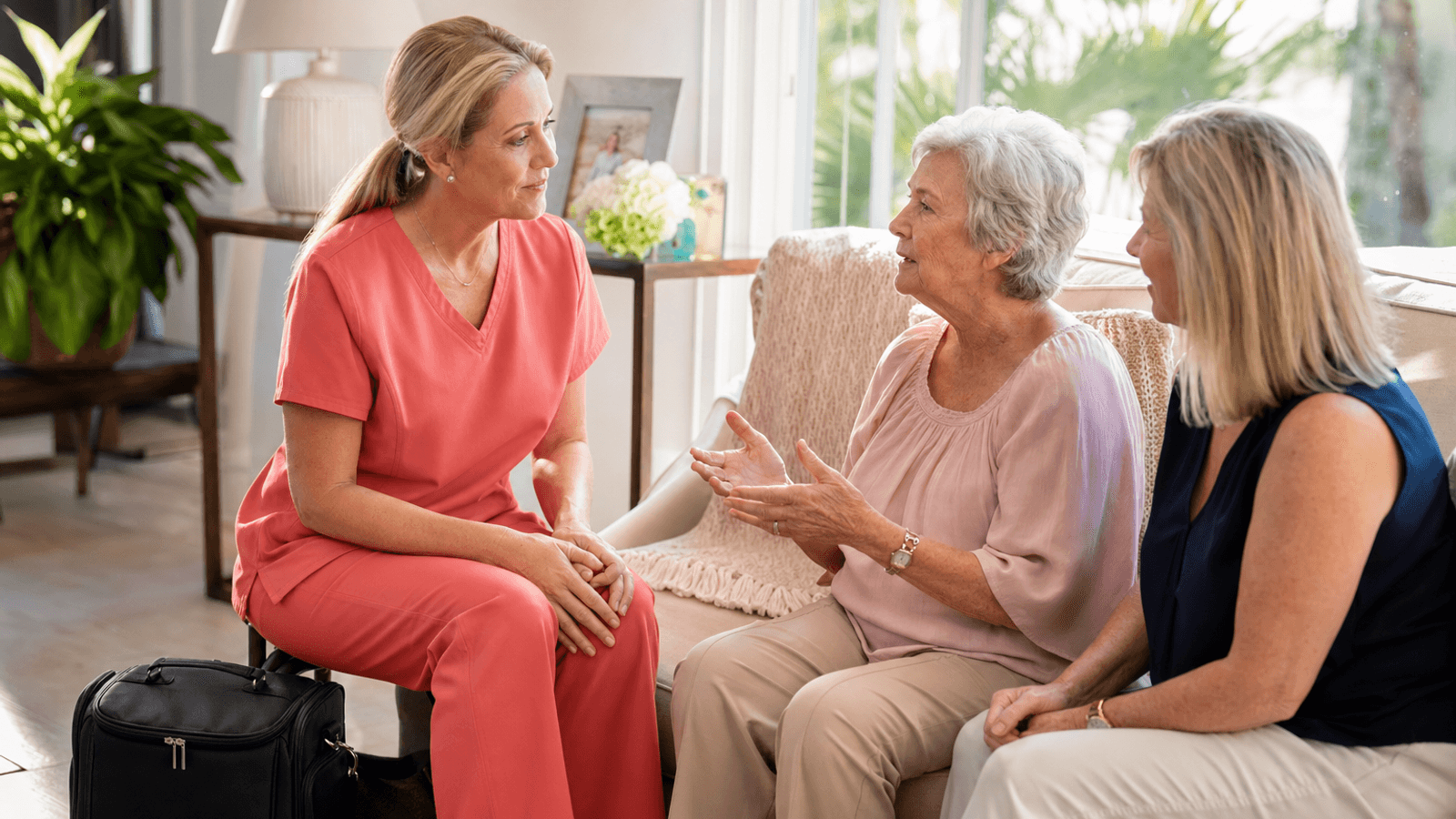 Hospice nurse in plain coral scrubs listening to a patient and family caregiver at home