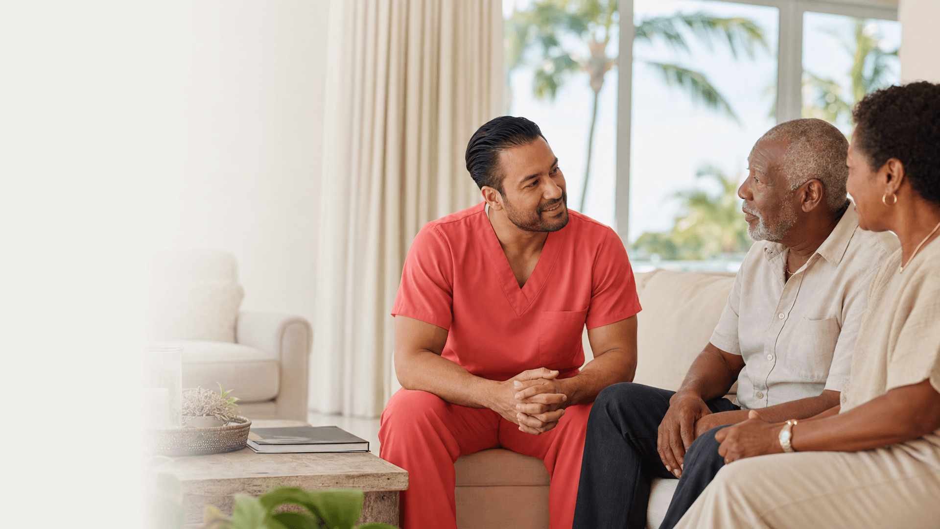 Hospice nurse in plain coral scrubs speaking with an older couple in their Florida home